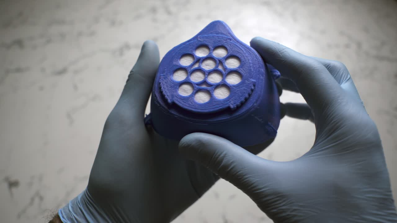 First person view of a male wearing surgical gloves assembling a 3D-printed homemade mask during the Covid-19 pandemic