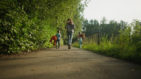 rear view of joyful mother running with kids on paved path surrounded by greenery, boy gripping teddy bear while sister runs alongside, sunlight casts soft shadows along quiet outdoor route