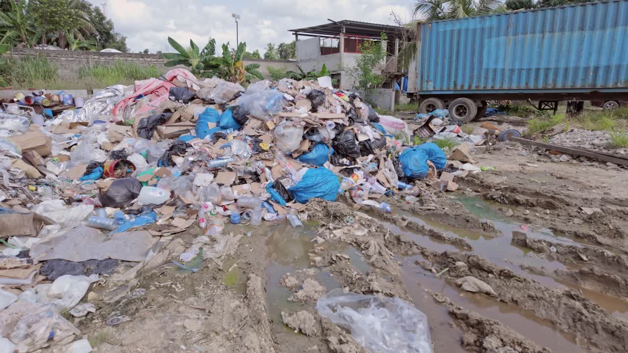 movimiento hacia adelante desde el nivel del suelo de un vertedero urbano en un día soleado, capturando agua sucia, plásticos desperdiciados, un contenedor abandonado, árboles y nubes en el cielo