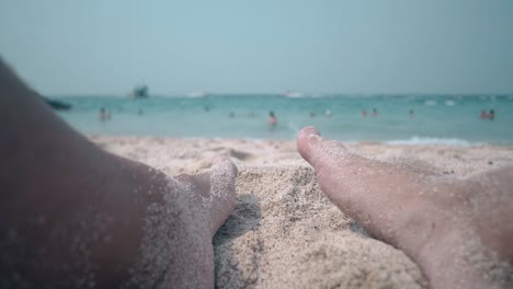 piernas en la arena en la playa contra el océano azul sin fin