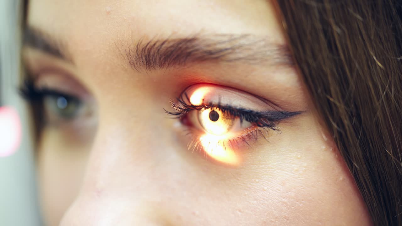 Young female checking her eyes at a doctor. Bright light shines inside the woman's eye. Concept of eye and cornea care. Close-up.