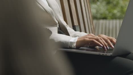 close up of businesswoman's hands on laptop keyboard as she sits outdoors in city gardens working 1