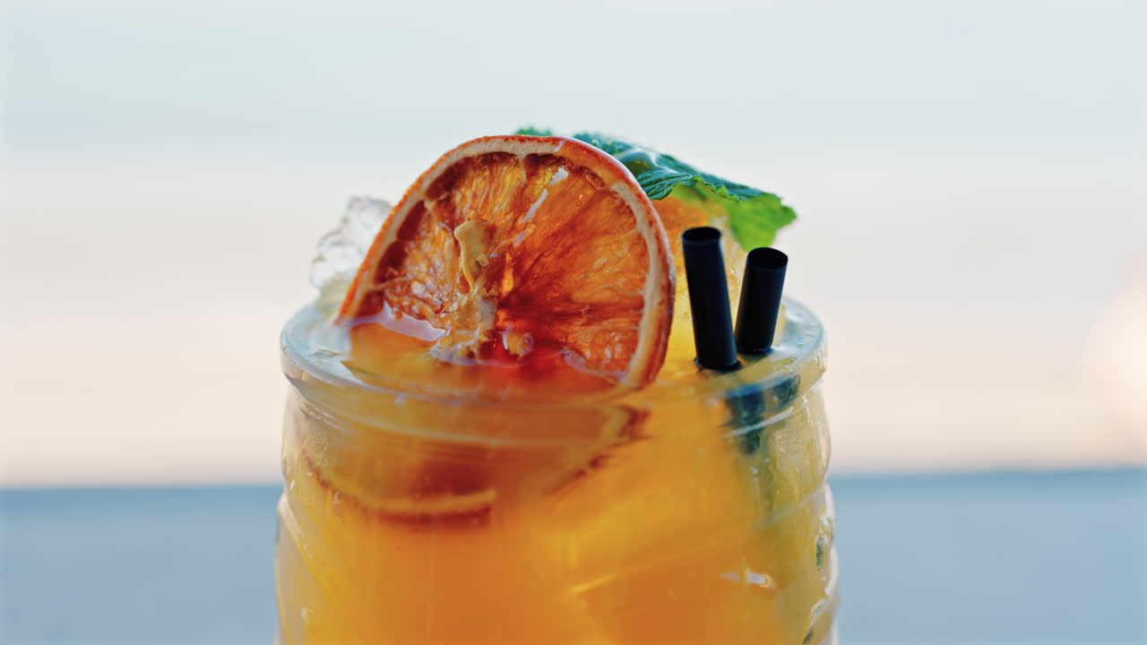 Close up of an orange cocktail on a table with a blurred view of the sea on the background