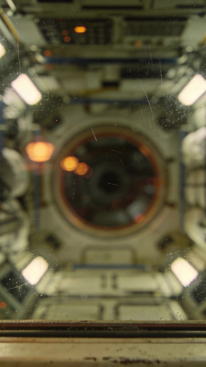 Vertical video: Camera filming dock hatch behind scratched window in module on boot, dust drifting