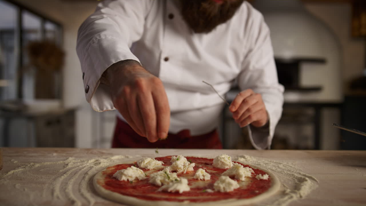 Kitchen chef cooking pizza in professional restaurant. Man adding spice on food.