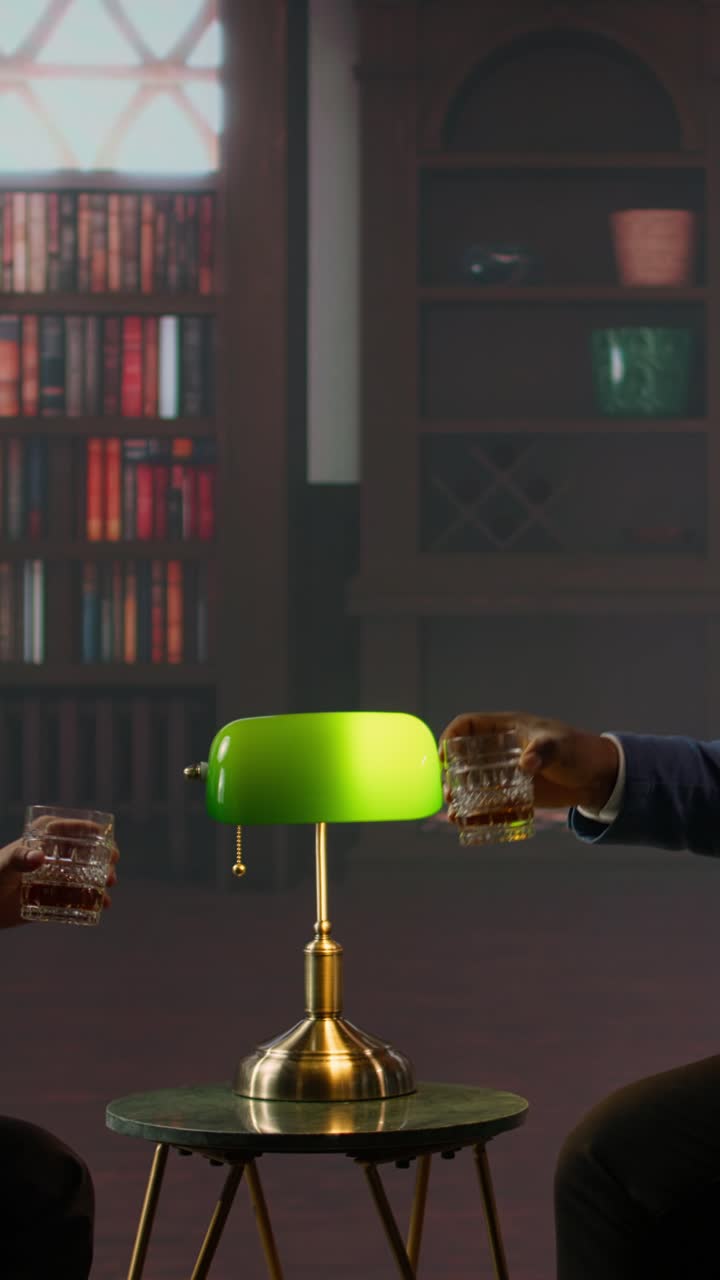 To personer skåler med whiskyglas i et klassisk biblioteksmiljø