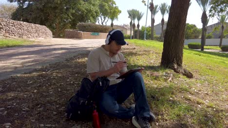 young man with headphones uses a tablet in a park.
