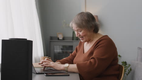 senior woman sitting at desk at home while using laptop