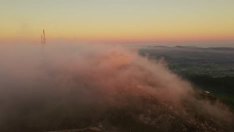 Filmische-Drohnenaufnahmen-Von-Wolken,-Die-Bei-Sonnenaufgang-über-Dem-Monte-Toro-In-Spanien-Aufleuchten-Und-Eine-Burgunterkunft-Auf-Einer-Klippe-Zeigen