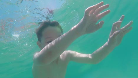 underwater shot, camera look up while young kid dives and submerge
