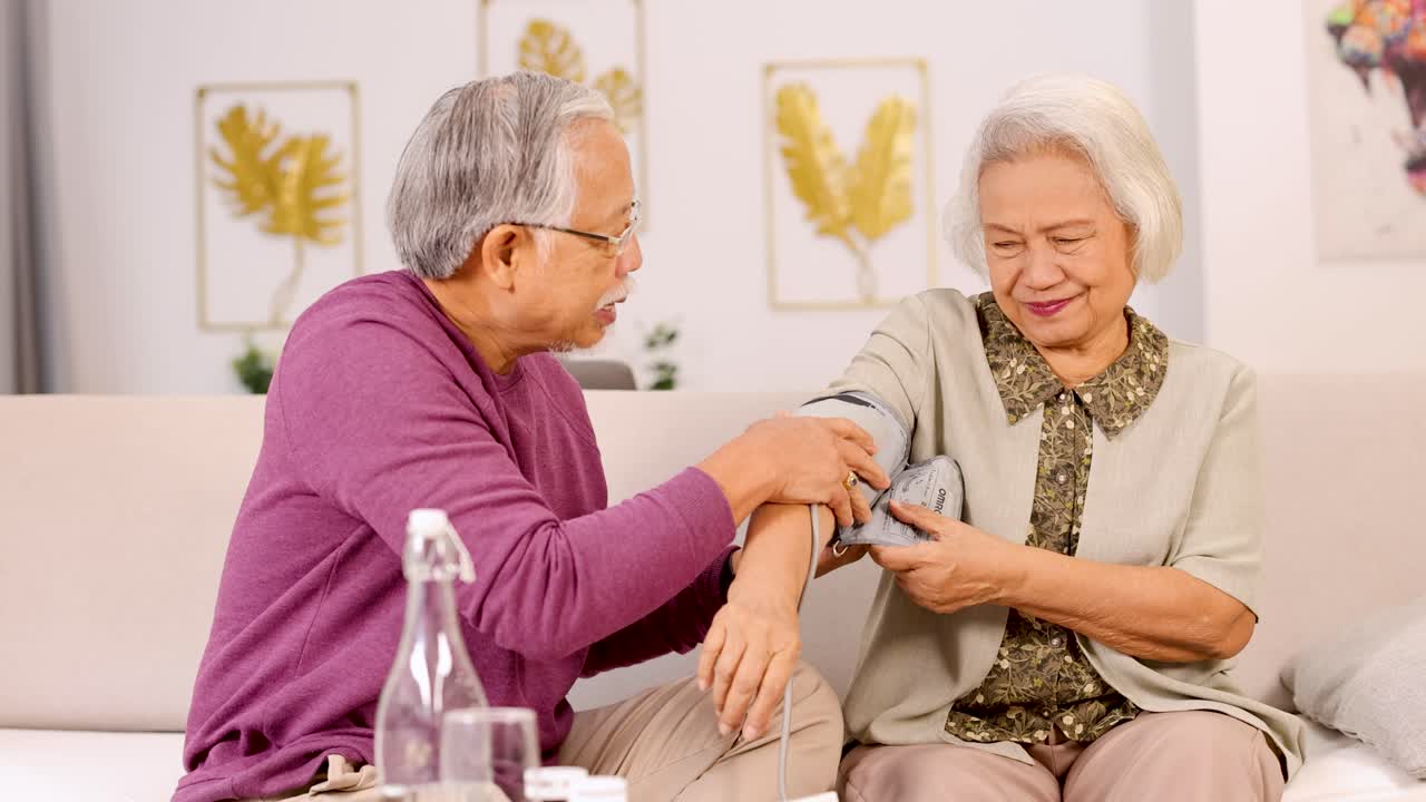 An elderly couple shares a loving moment while checking blood pressure in a cozy, well-lit living room