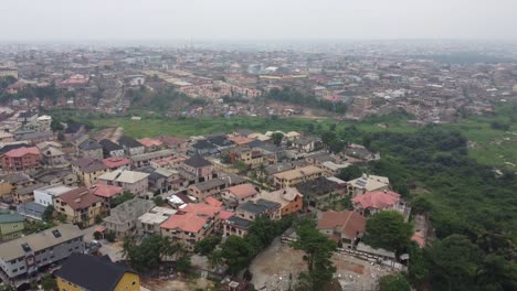 Vista-Aérea-Del-Vecindario-En-Lagos-Nigeria-En-Un-Día-Brumoso-Con-Drones-Cayendo-Para-Revelar-Una-Vegetación-Verde-Al-Lado-Del-Vecindario