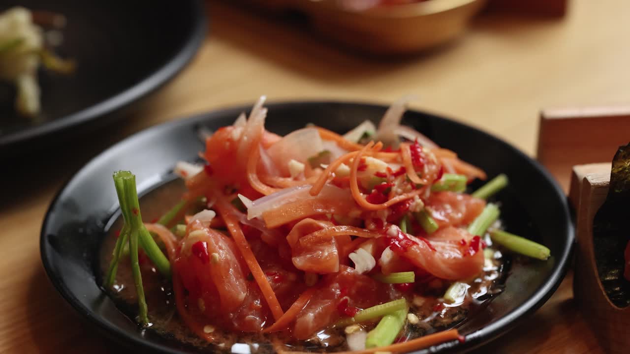 Chopsticks pick up spicy raw salmon salad with vegetables in warm, soft restaurant lighting, close-up