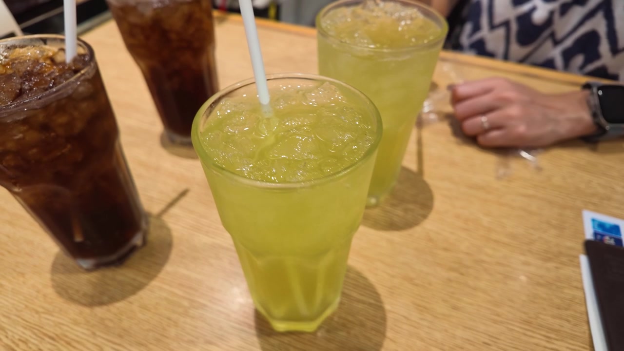 Close-up high angle shot of cold beverages with ice and straws on wooden table.