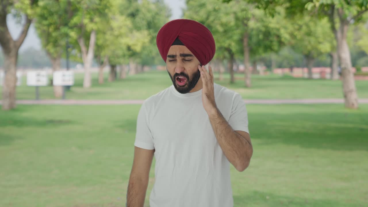 Uomo indiano sikh malato che soffre di mal di denti nel parco
