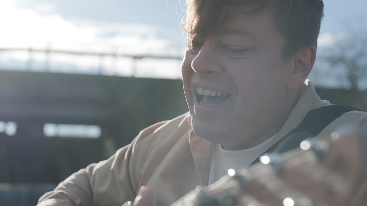 바위의 배경에 산의 강변에 앉아 기타를 연주하는 젊은이. 자유의 개념, 휴식 장소.