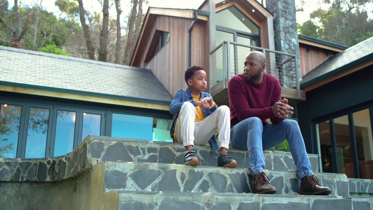 African American father and son on stone steps son fidgeting phone leading dad leaning and nodding
