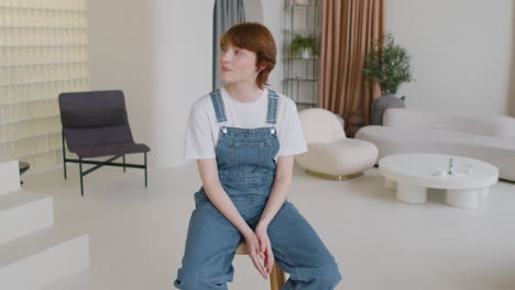 girl in denim jumpsuit sitting on banquette and looking at camera and smiling in the middle of the living room of a modern house 1