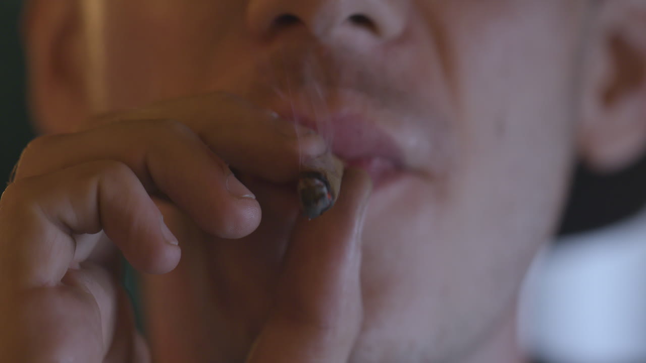 un primer plano macro de un hombre fumando un porro y luego sonríe