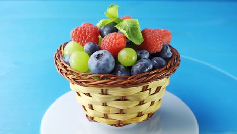 rotating wooden basket with different forest berries close-up on a blue wooden table. 4k slow motion loop video with speed ramp effect.