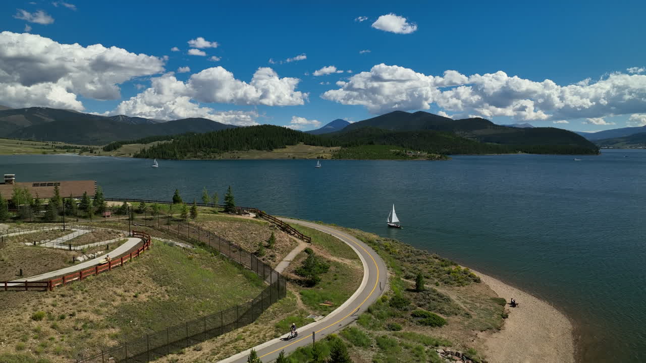 Aerial cinematic drone Breckenridge ski resort Keystone bikes path sailing boats Lake Dillon Colorado 9 mile range summer blue sky clouds daytime Frisco Silverthorne Reservoir dam down motion
