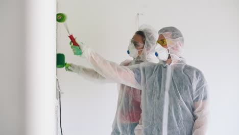 man and woman in transparent coveralls paint room white wall