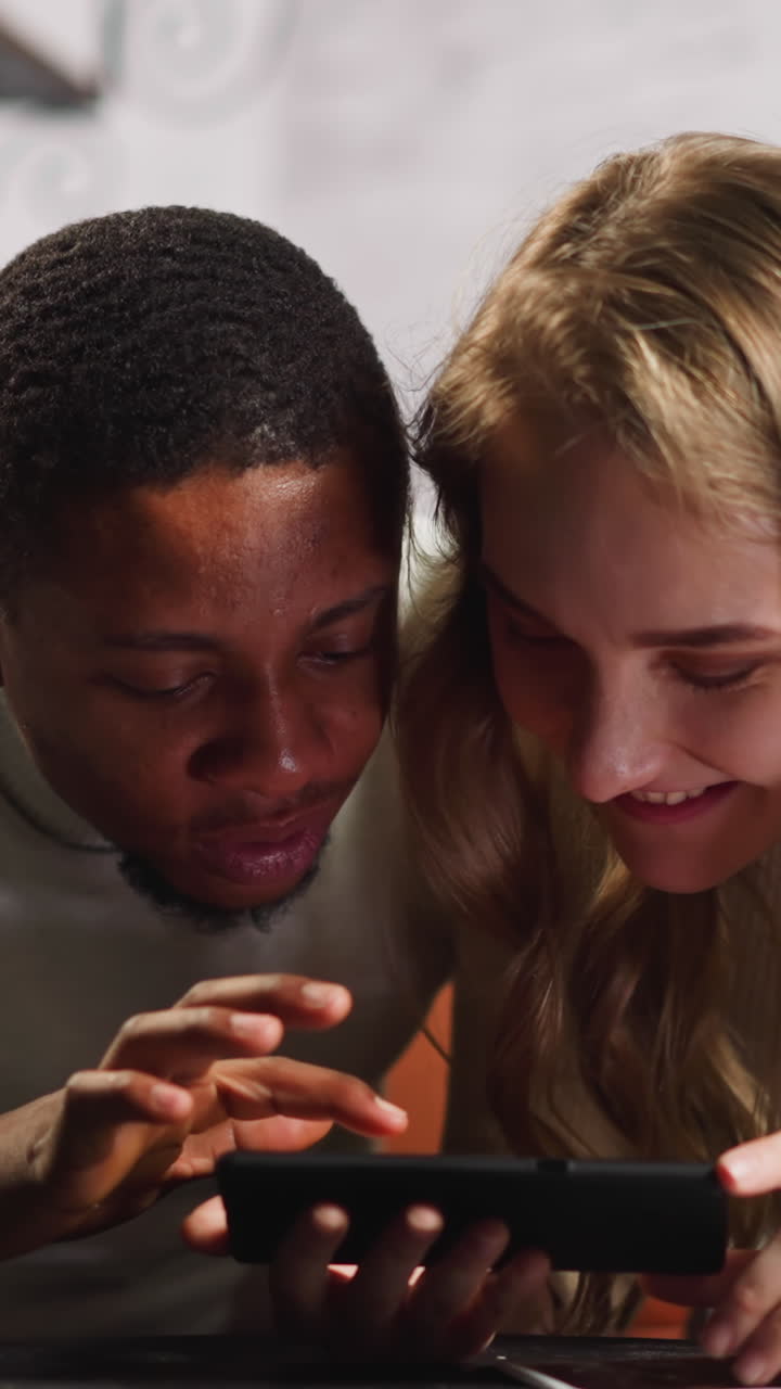 Amazed African-American man with beloved white pregnant wife watches ultrasound recording of unborn child via smartphone in living room slow motion