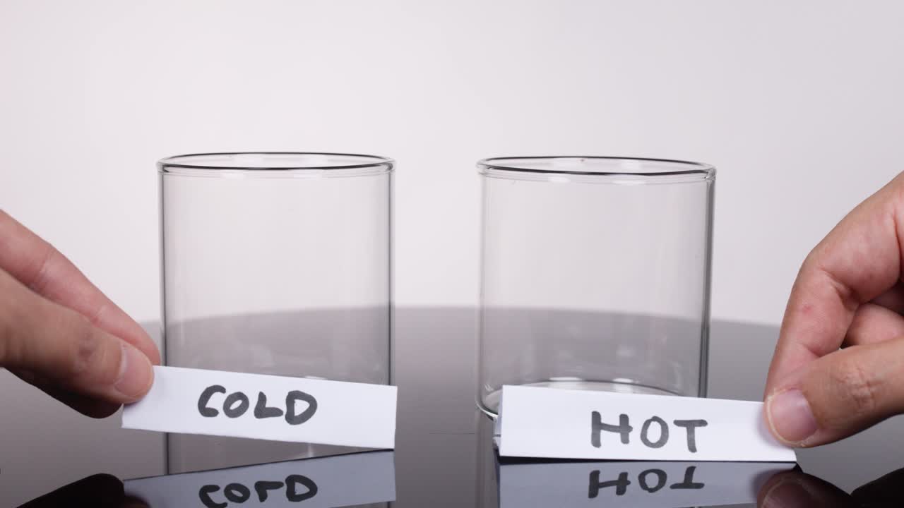 Hands place cold and hot paper labels before two empty glass cups on reflective surface