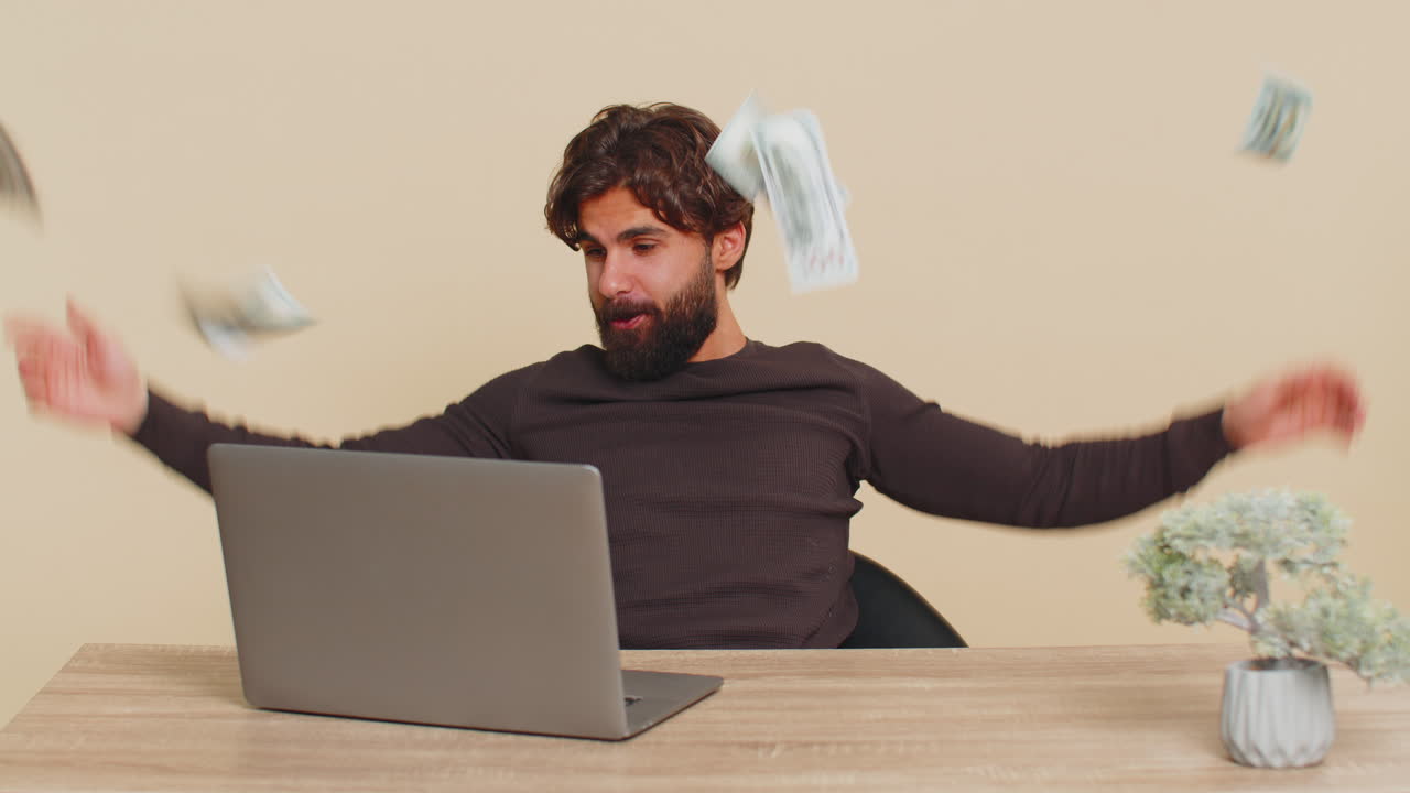 현금 달러 비가 테이블에 앉아 베이지 바탕에 성공을 축하하는 남자에게 떨어집니다.