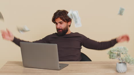 money cash dollar rain falling on man sitting at table celebrating success against beige background