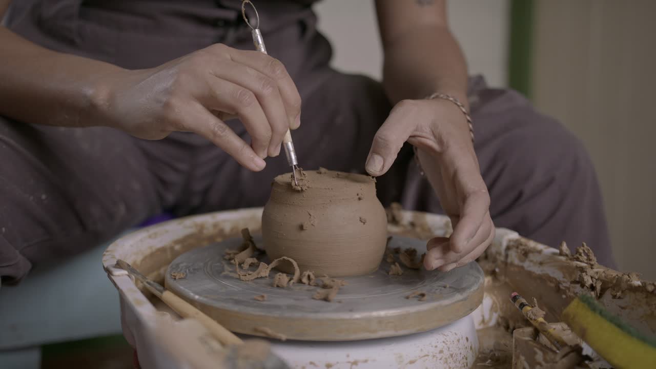 Vasaio utilizza con cura un attrezzo a nastro per rifinire il taglio di un vaso di argilla rotante SLOW MOTION.