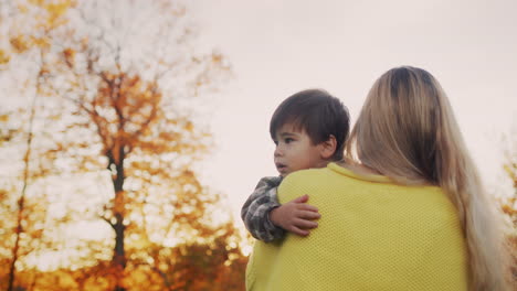 mom carries a baby in her arms, walks through a beautiful park at sunset