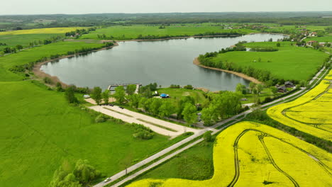 Vista-Aérea-Del-Lago-Wielochowskie-Y-Sus-Alrededores,-Incluidos-Campos-Verdes,-Campos-De-Colza-Amarillos-Y-Una-Carretera,-Con-Una-Vista-Panorámica-Del-Campo.