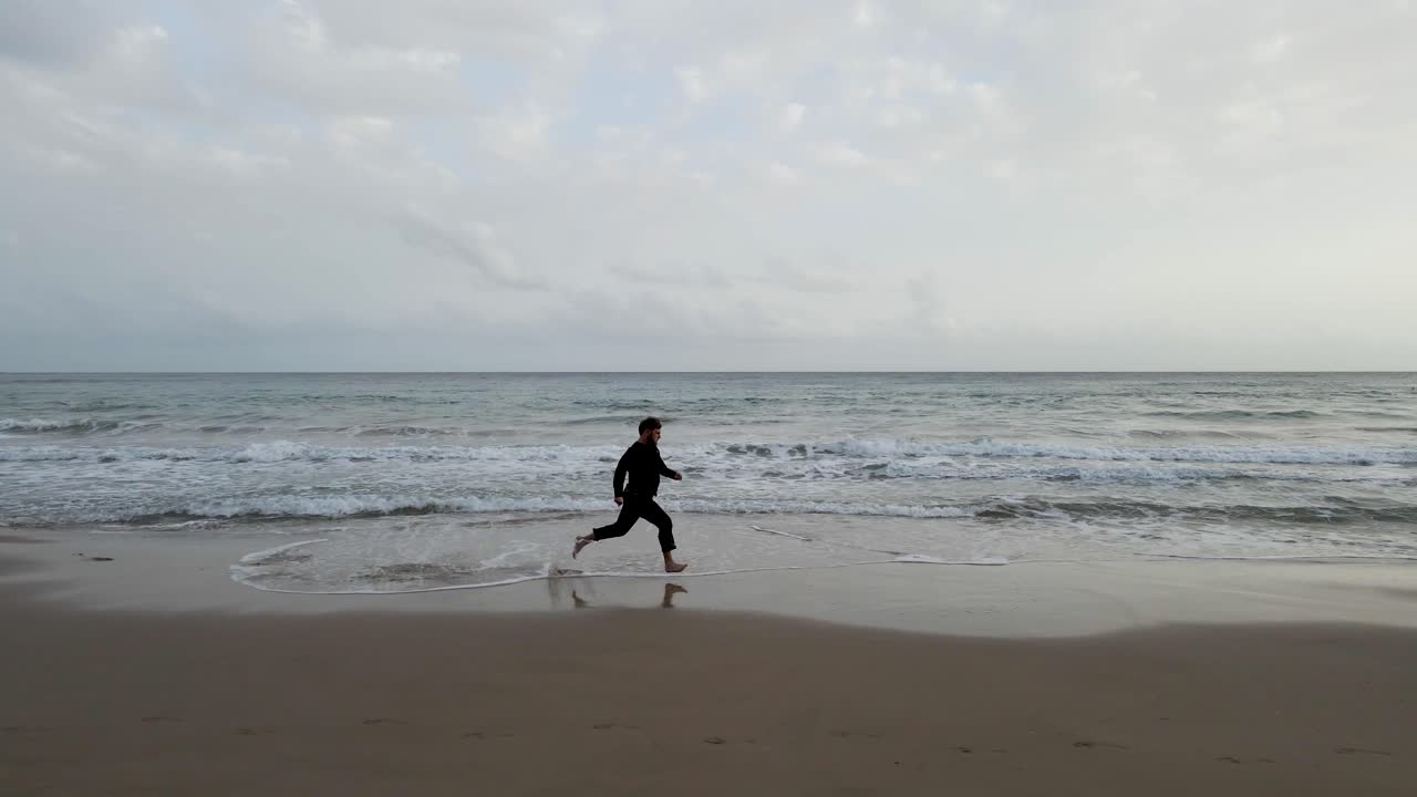 A lone man runs along the beach in Calpe, Spain, near the water's edge, creating a serene and meditative atmosphere
