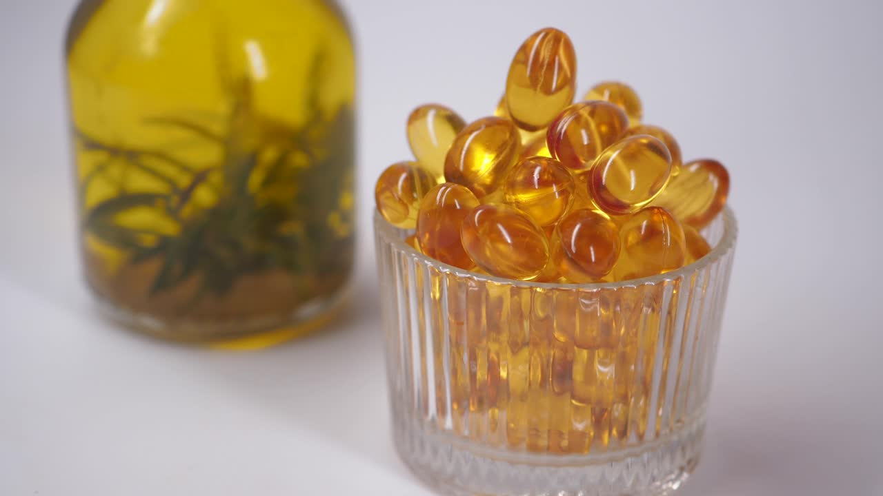 Mano che raccoglie capsule dorate accanto a un flacone di olio alle erbe