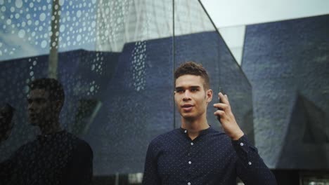 well-dressed entrepreneur businessman portrait of a young attractive trendy man talking on the cell phone mobile on a sunny morning day with a modern urban city background in slow motion