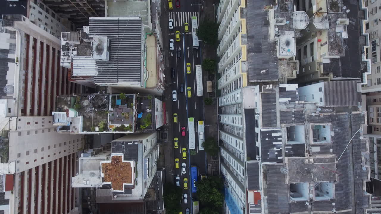 Toma de dron vertical moviéndose a lo largo de una calle concurrida en Río de Janeiro, mostrando tráfico denso con muchos coches amarillos entre edificios altos.