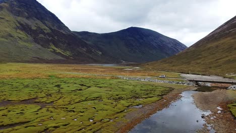 push-in drone shot of scottish mountain valley with car passing by