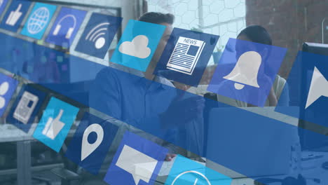 coworkers collaborating at modern office desk, viewing laptop screen with floating it icons overlay