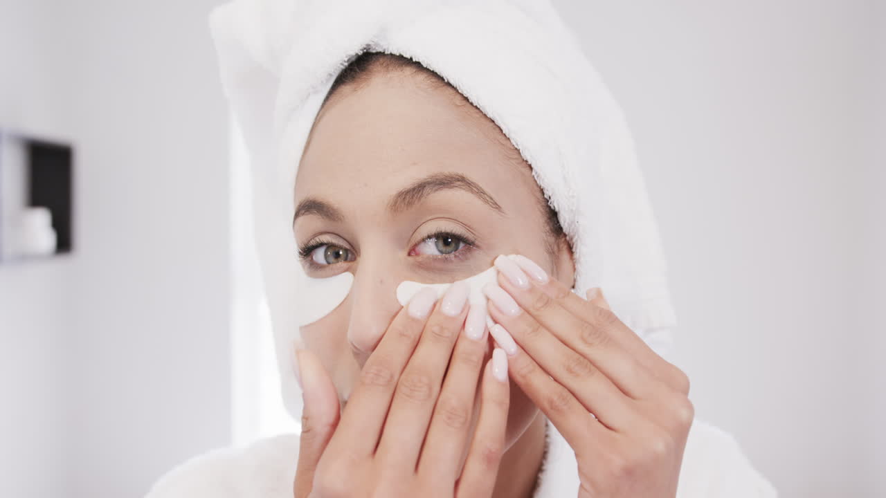 retrato de una mujer biracial aplicando parches debajo de los ojos en el baño, cámara lenta