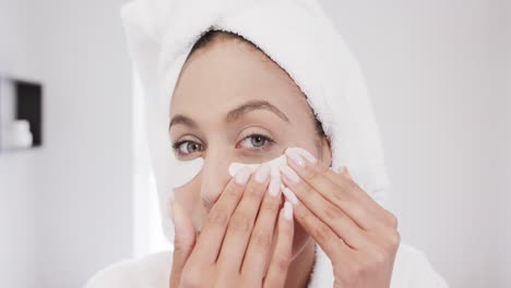 Portrait-of-biracial-woman-applying-under-eye-patches-in-bathroom,-slow-motion