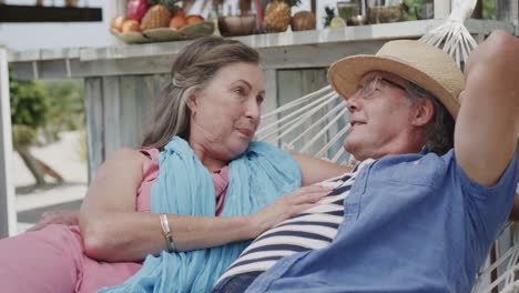 una feliz pareja caucásica anciana acostada en una hamaca hablando fuera del bar de la playa, en cámara lenta.