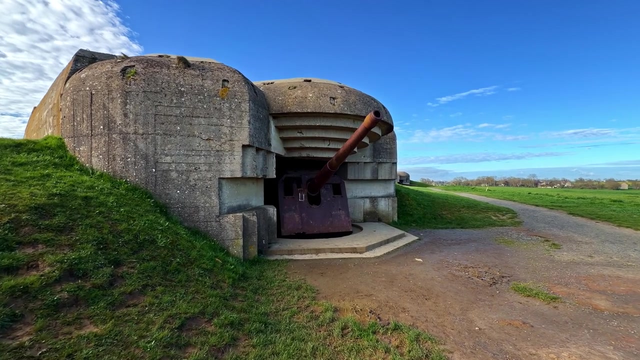 Historisk kystbatteri fra andre verdenskrig i Longues-sur-Mer i Normandie, Frankrike, med naturskjønn himmel og gresskledd landskap