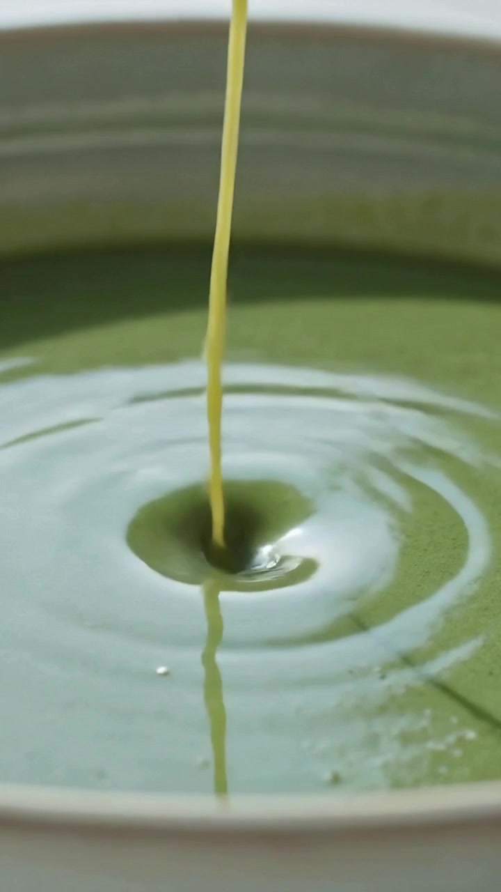 Video verticale: Versando dal bordo di un cucchiaio, rilasciando un liquido verde viscoso in una ciotola di ceramica