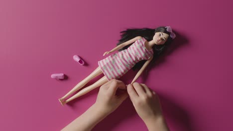 Overhead-Aufnahme-Eines-Mädchens,-Das-Eine-Spielzeugpuppe-Auf-Rosa-Hintergrund-Spielt-Und-Verkleidet