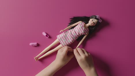 overhead shot of girl playing and dressing up toy doll on pink background