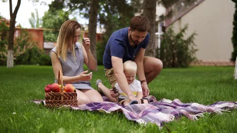 happy family concept. mother and son are sitting on plaid, enjoing picnic outdoors. father brings some cones for his son. picnic basket. green park. slow motion