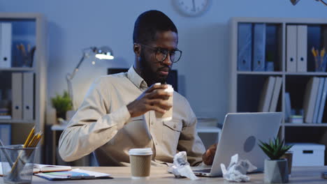 young man working with laptop and drinking coffee in the office at night