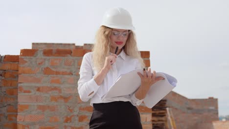 female architect in business attire standing outdoors at construction site. the architect makes marks in the architectural plan