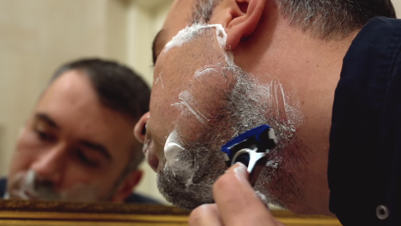 Close de um homem se barbeando em frente ao espelho no banheiro
